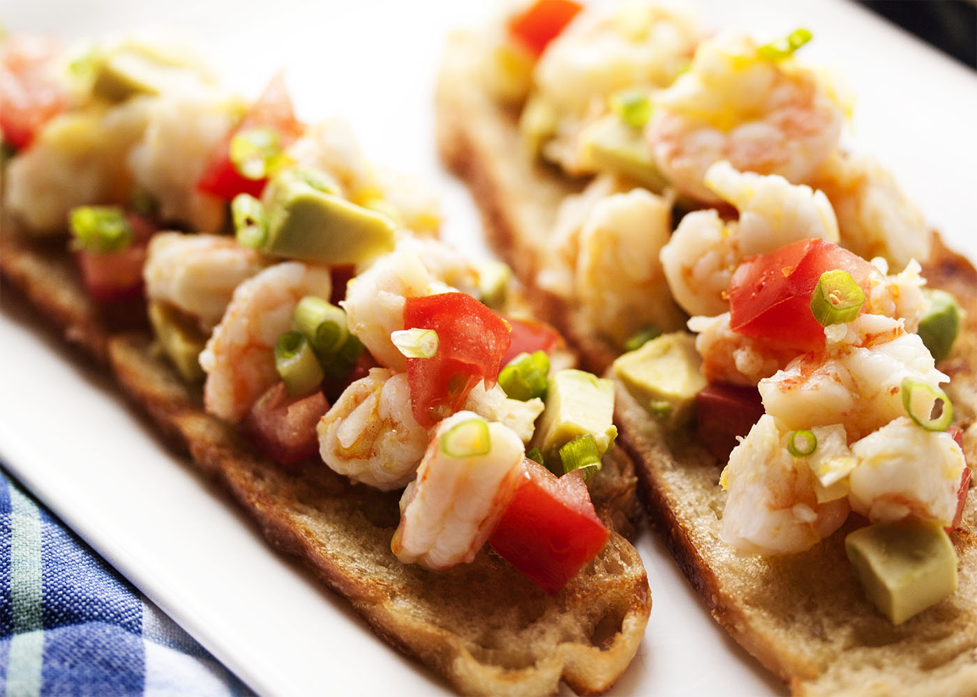 Tomato and Avocado Shrimp Crostini - Beautifully poached shrimp are marinated in lemon and olive oil and paired with grilled bread, diced tomato, and avocado in this Shrimp Crostini. Poaching keeps the shrimp tender and infuses them with flavor. So good! | justalittlebitofbacon.com