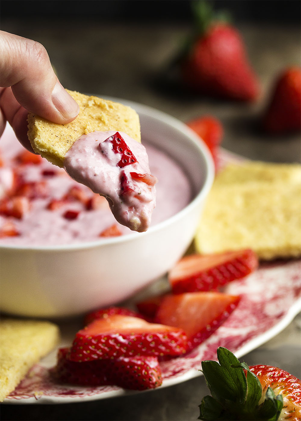 Strawberry cheesecake dip on a shortbread cracker with the bowl of dip in the background.