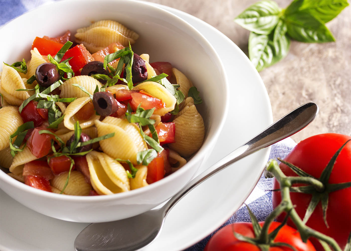 A bowl full of pasta shells tossed with raw tomato sauce, along with lots of kalamata olives and fresh basil.