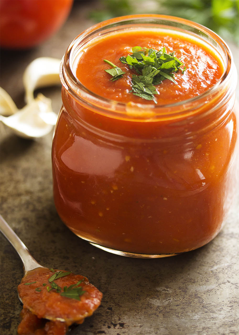 My authentic Italian marinara sauce filling up a glass jar with some fresh, chopped parsley sprinkled on top of the sauce.