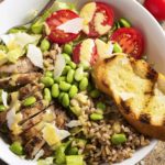 Caesar salad becomes satisfying meal in a bowl with the addition of spicy grilled chicken thighs, farro, tomatoes, and edamame. | justalittlebitofbacon.com