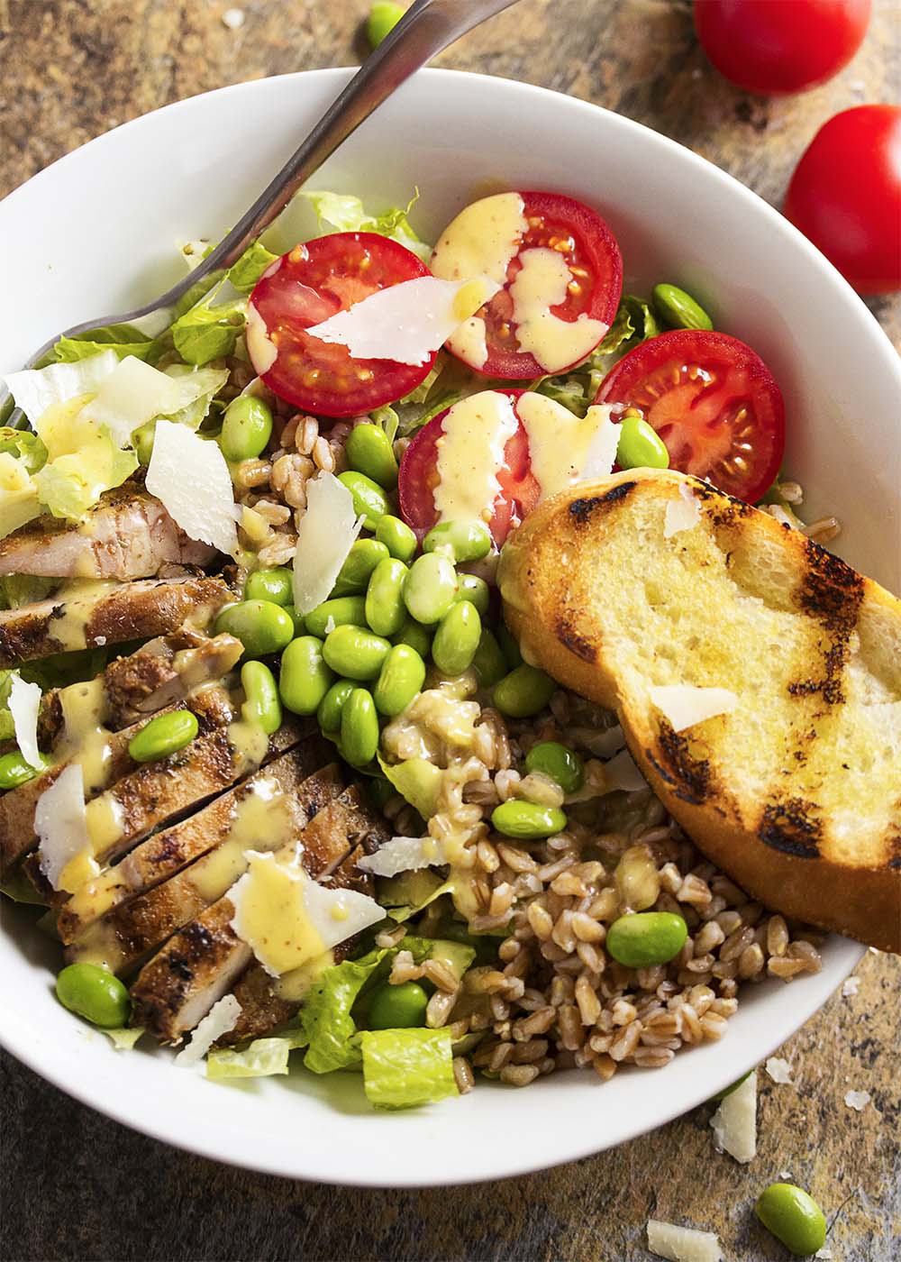 Caesar salad becomes satisfying meal in a bowl with the addition of spicy grilled chicken thighs, farro, tomatoes, and edamame. | justalittlebitofbacon.com