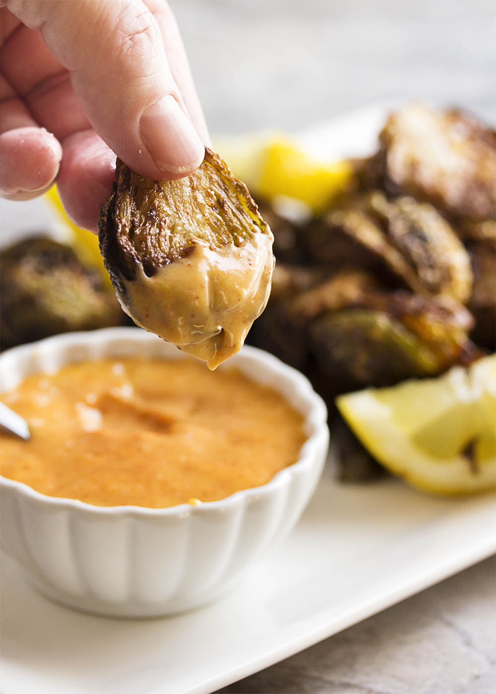 A hand holding up a crispy deep fried Brussels sprout which has been dipped in the sweet and spicy maple aioli.