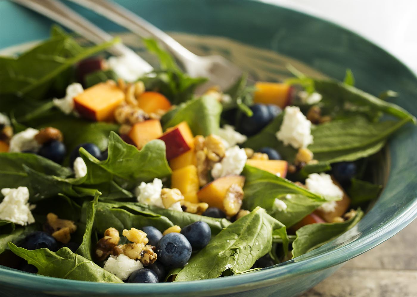Punch up your spinach salad with seasonal summer fruits, creamy cheese, and glazed walnuts in this peach and blueberry spinach salad. | justalittlebitofbacon.com