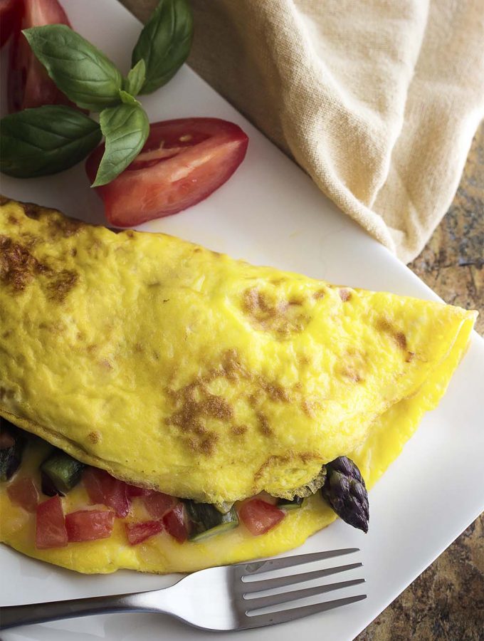 Take advantage of fresh asparagus to make a healthy spring omelette! This asparagus omelette is full of smoked gouda cheese, sauteed onions, and tomatoes. Great for breakfast, brunch, or even dinner. | justalittlebitofbacon.com