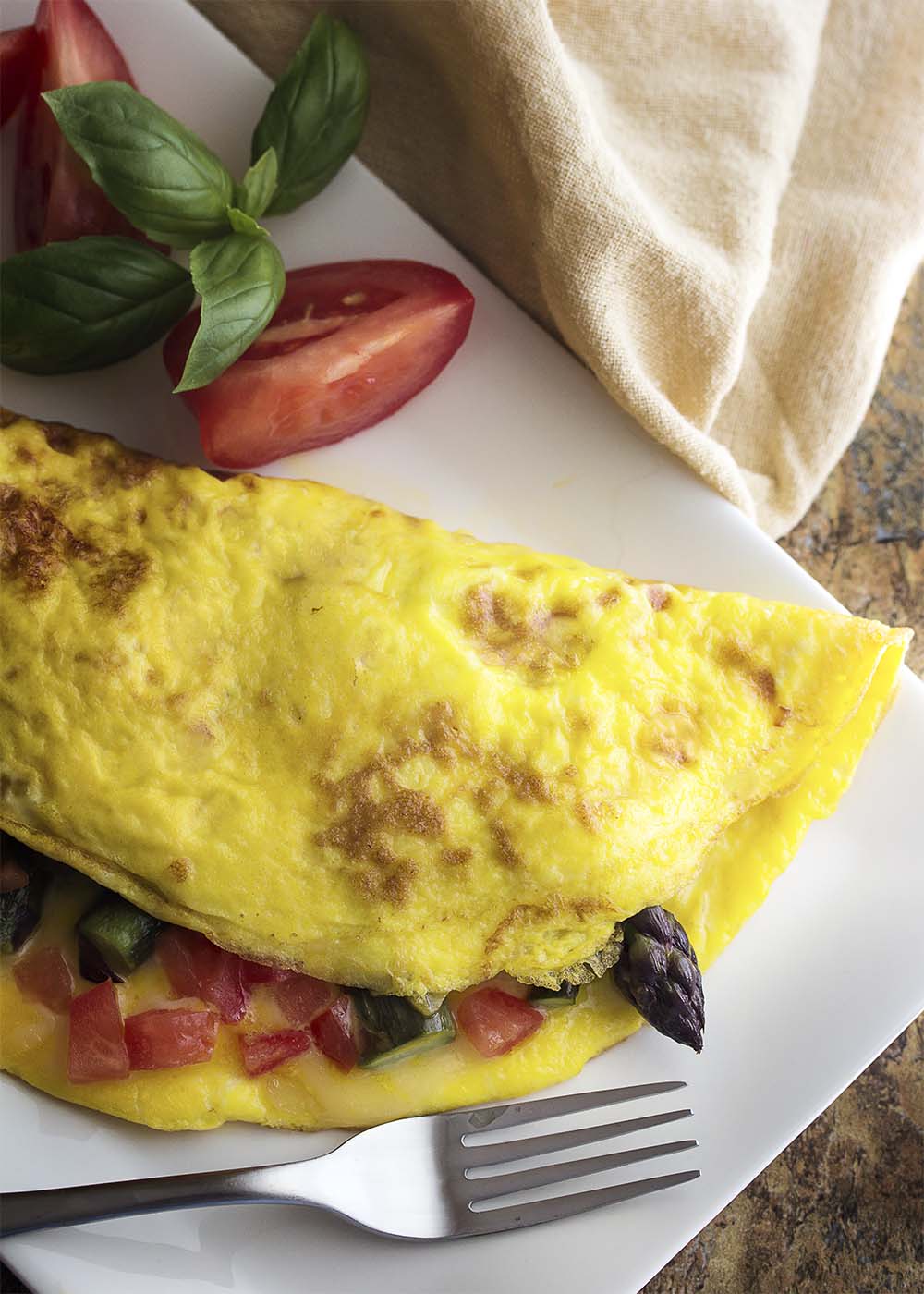 Take advantage of fresh asparagus to make a healthy spring omelette! This asparagus omelette is full of smoked gouda cheese, sauteed onions, and tomatoes. Great for breakfast, brunch, or even dinner. | justalittlebitofbacon.com
