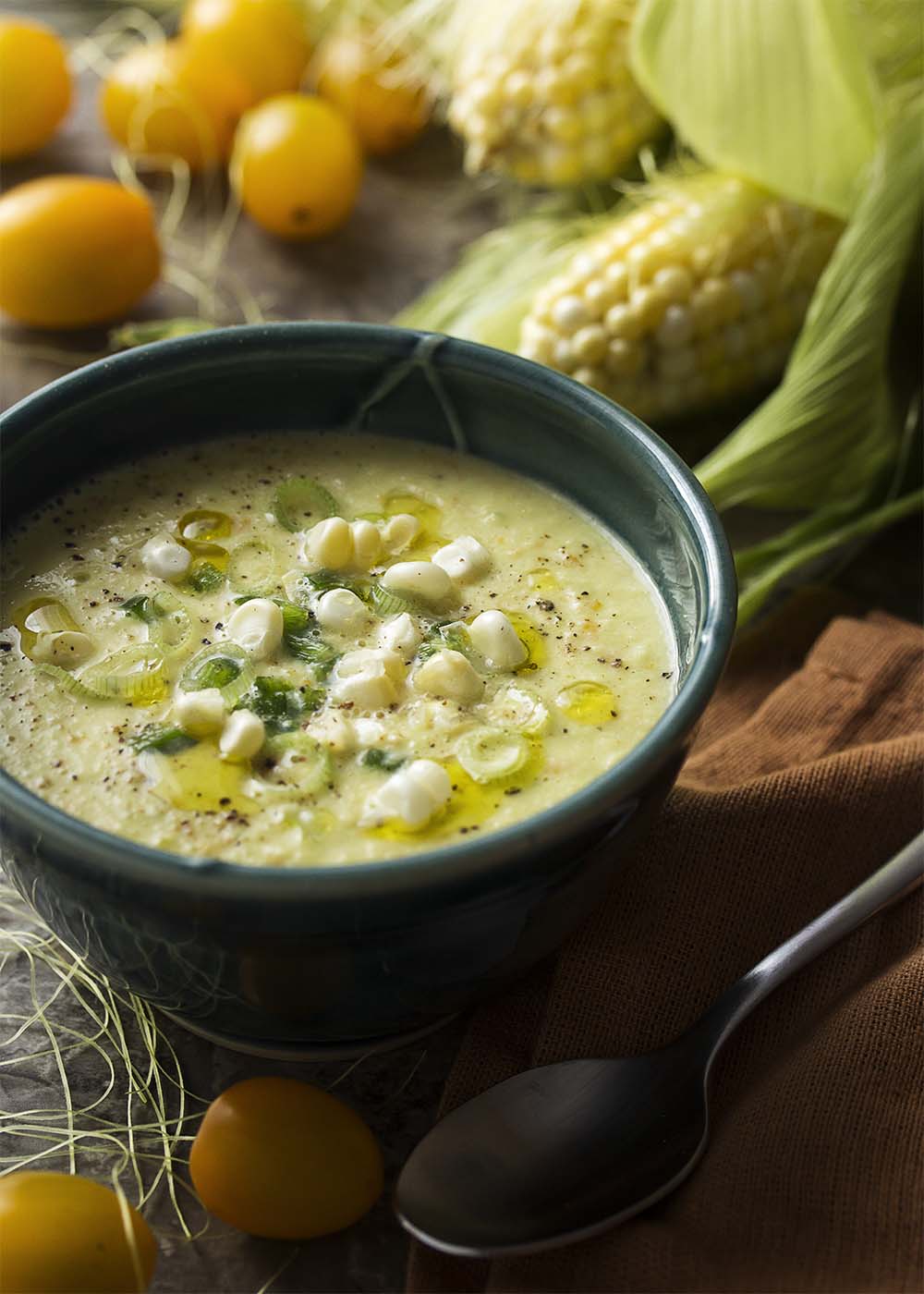 Rustic green bowl of sweet and spicy corn gazpacho topped with corn kernels, jalapenos, and sliced scallions.