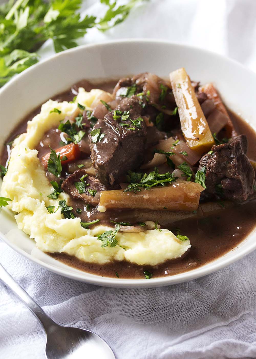 White bowl of mashed potatoes topped with beef burgundy stew.