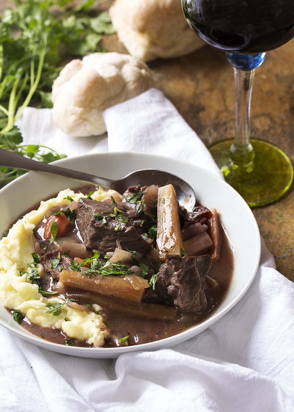 White bowl with a spoon of mashed potatoes and beef burgundy.