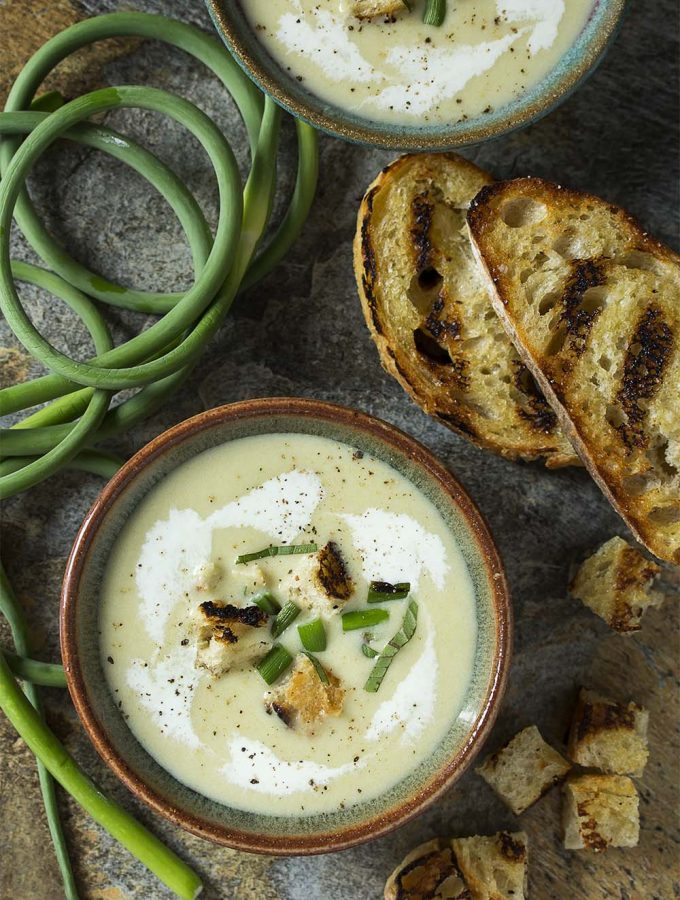 Wondering how to use garlic scapes? A great way to use them is to make a cold garlic scape soup! Perfect for summer and easy to make ahead. Scapes and leeks sauteed in butter and simmered with potatoes make a great twist on the classic French vichyssoise.