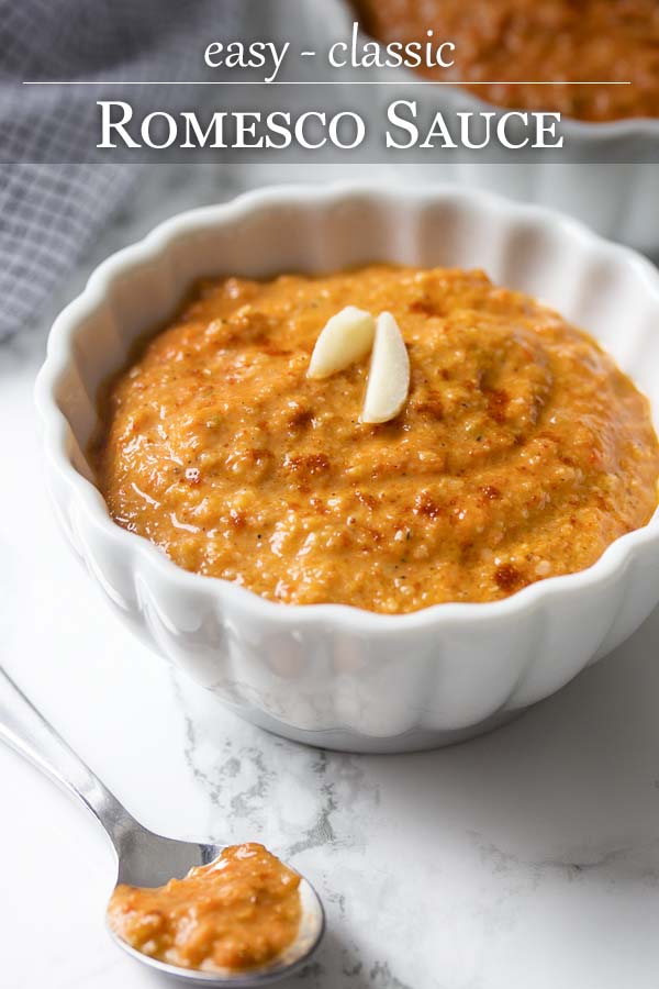 Red sauce in a small white bowl with text overlay - Classic Romesco Sauce.