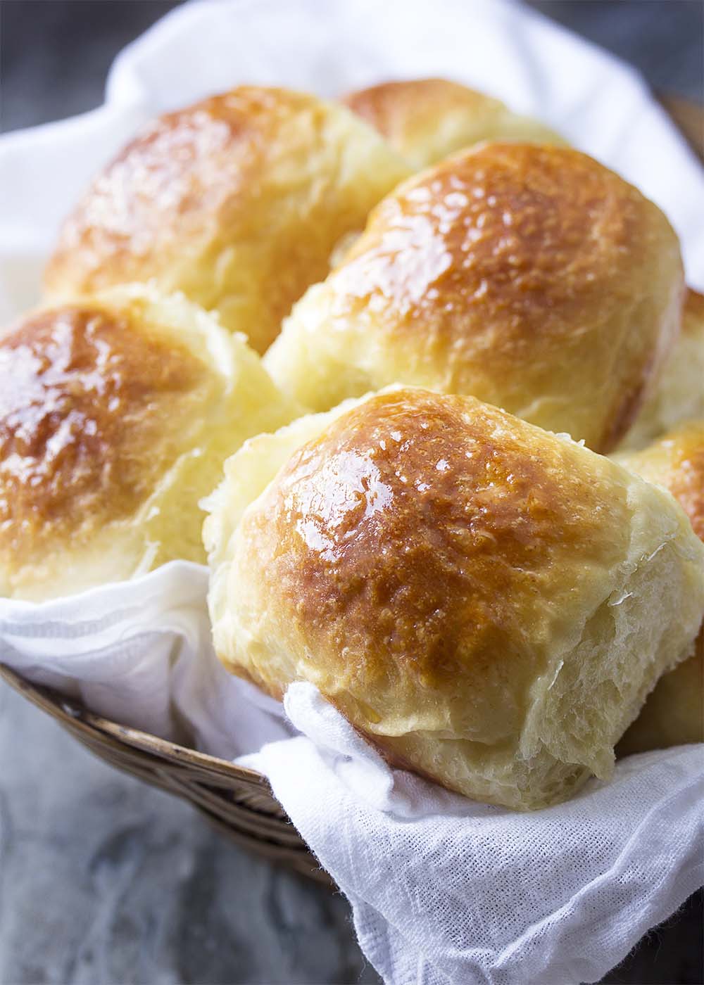 A basket lined with a white cloth and filled with soft and fluffy no-knead dinner rolls.