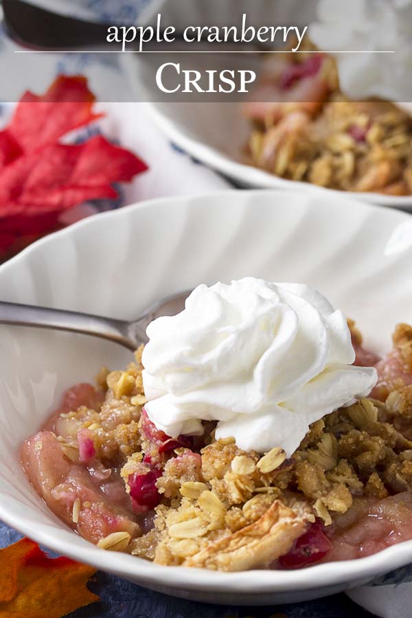 White bowl of dessert topped by whipped cream with text overlay - Apple Cranberry Crisp.