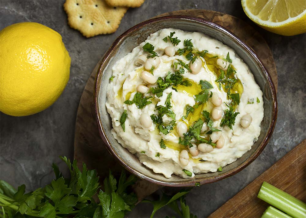 Top view of bean dip in a small bowl, all swirled with parsley and olive oil. 