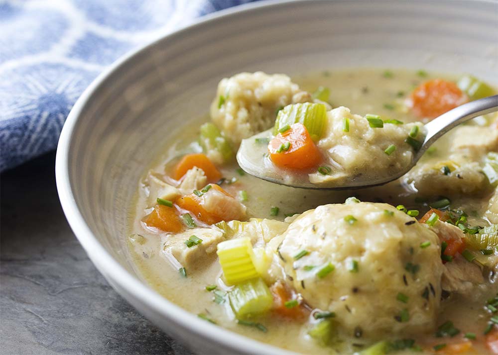 A spoon lifting up some soup over a bowl of chicken and dumplings.