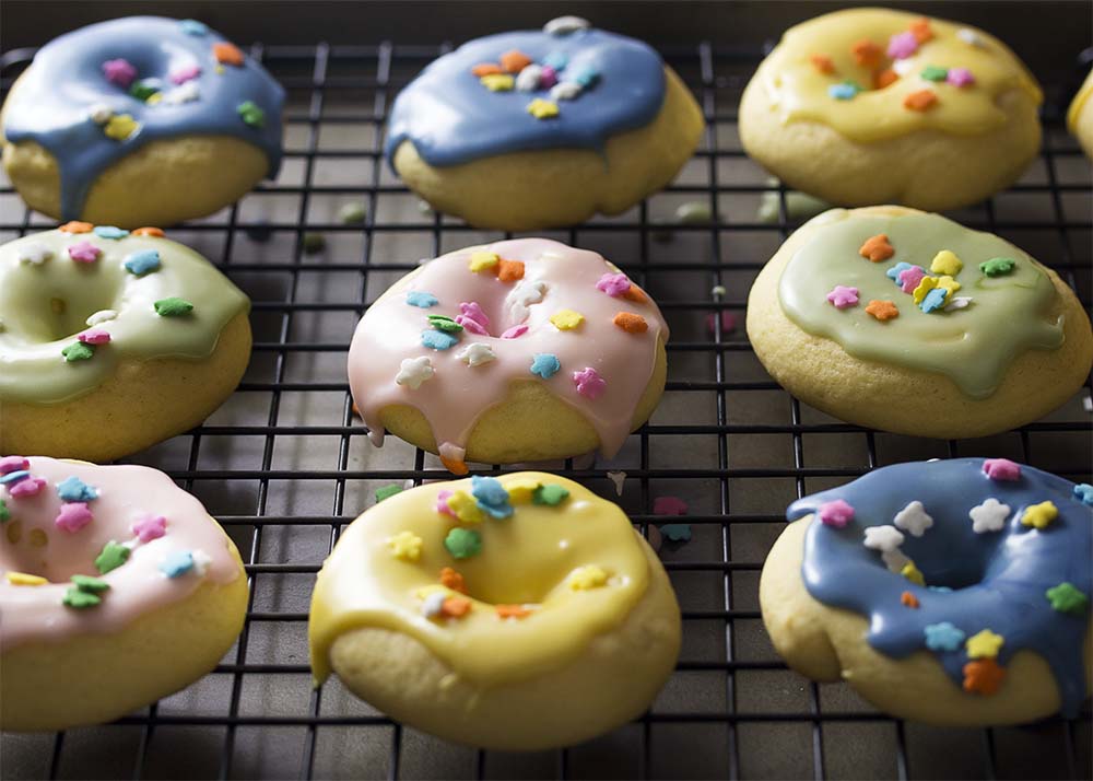 Cookies glazed in colorful pastel icing arranged in rows on a cooling rack.