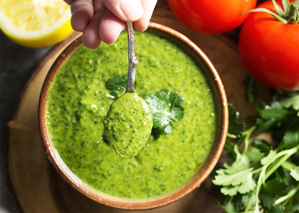 A spoon of Italian salsa verde held up over a bowl of the sauce.