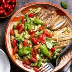For an easy and healthy cold summer or spring dinner, make chicken pesto pasta salad! It's full of the fresh flavors of tomatoes, basil, and asparagus along with simple grilled chicken thighs. Can be served warm or made ahead for a bbq or picnic. | justalittlebitofbacon.com #saladrecipes #italianrecipes #pastasalad #pesto #summerrecipes #grilledrecipes