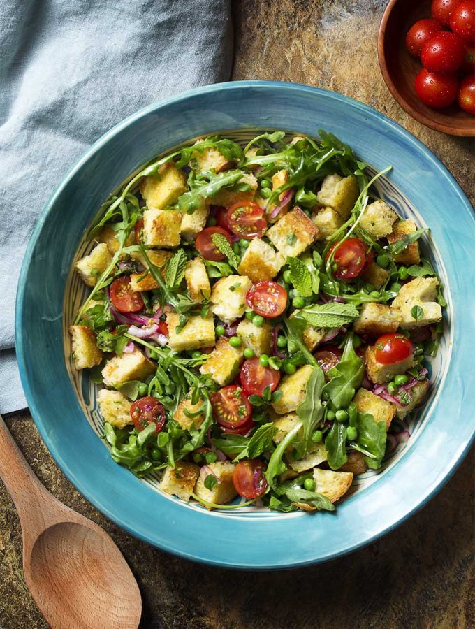 For a fresh take on Italian bread salad, make a spring panzanella salad with peas, arugula, mint, and cherry tomatoes all tossed in a bright, lemony dressing. | justalittlebitofbacon.com #saladrecipes #italianrecipes #panzanella #tomatobreadsalad #springrecipes