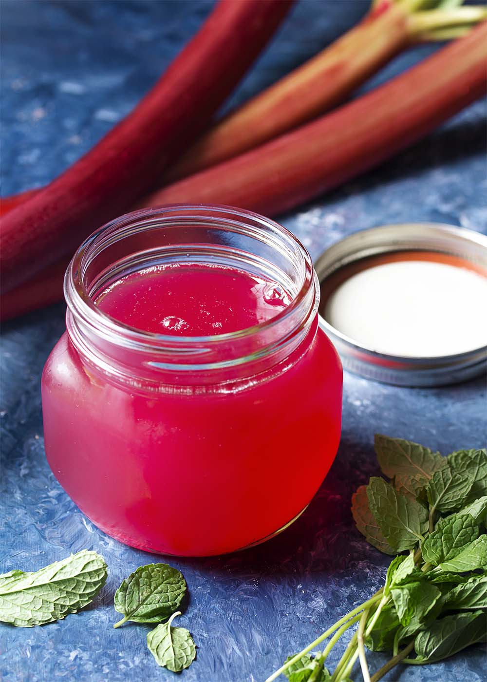 A glass jar of rhubarb syrup showing the deep pink color of the syrup.