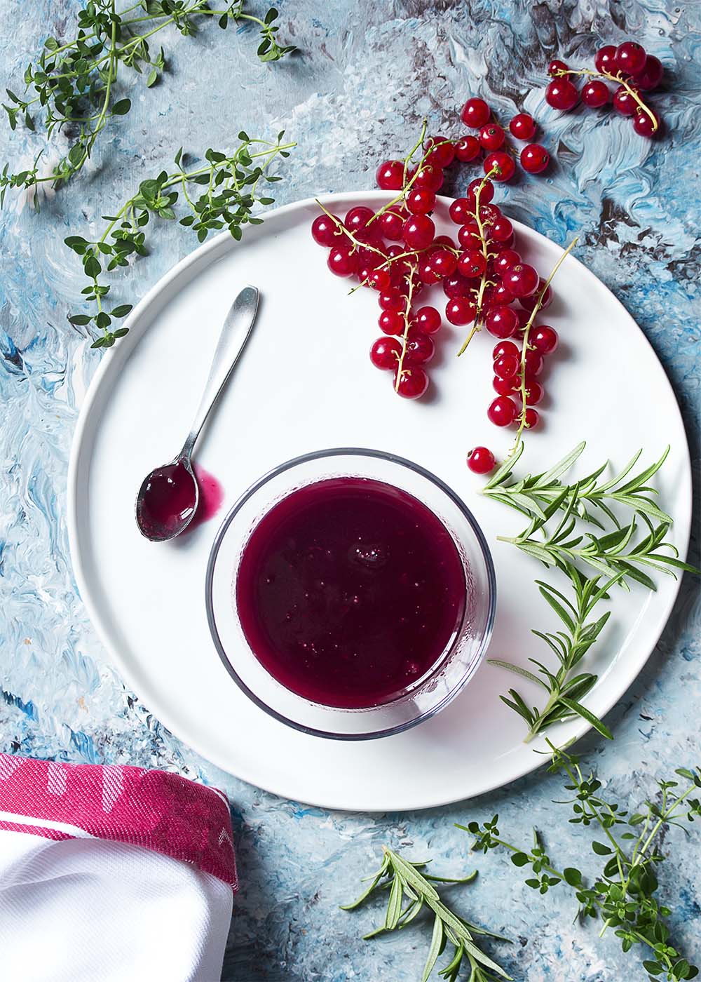 Top view of a cup of red currant sauce on a white plate with a spoon.