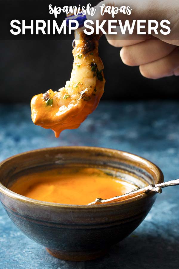 A hand holding up a grilled shrimp and sauce with text overlay - Shrimp Skewers.
