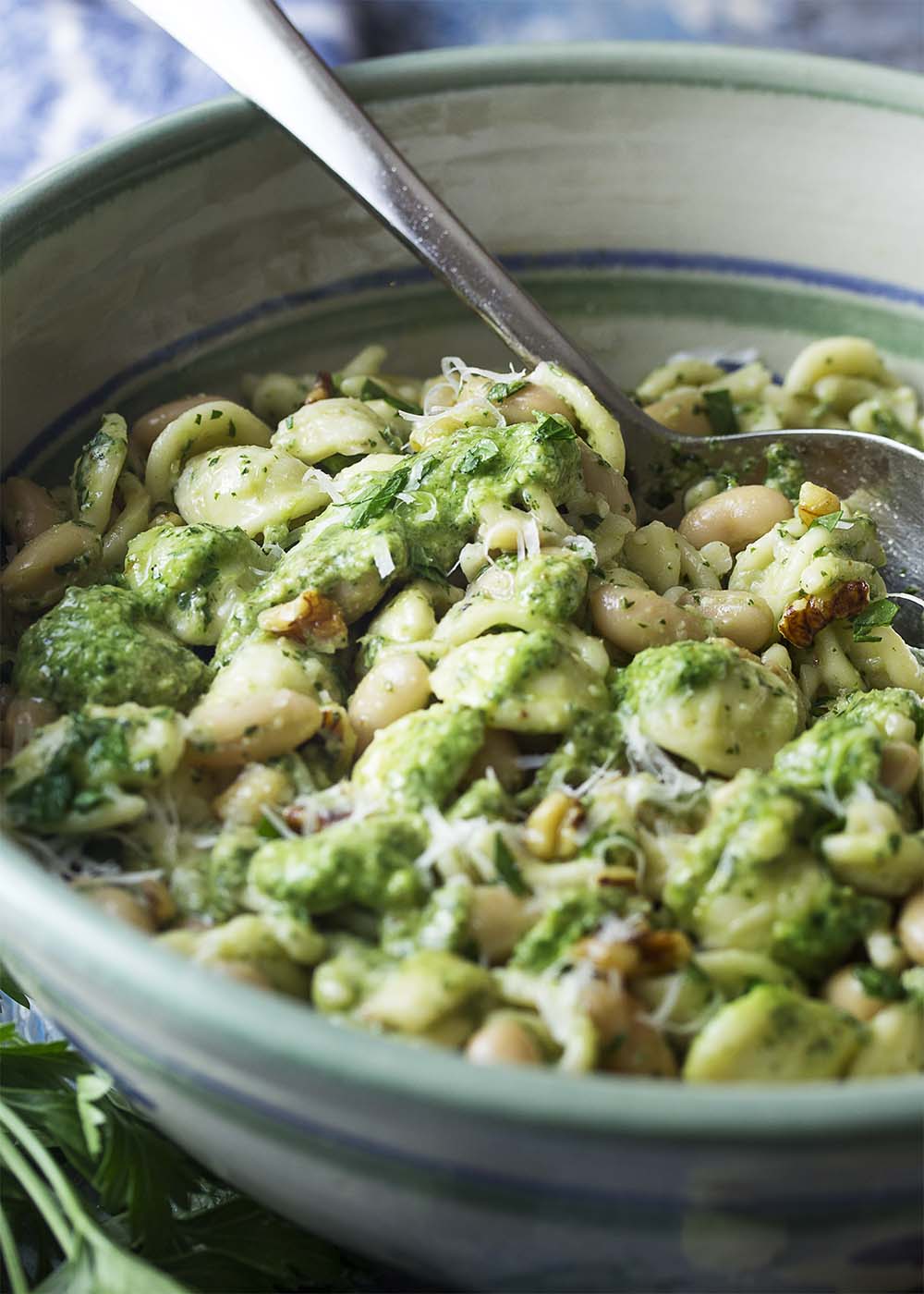 A large serving bowl of orecchiette and beans tossed with pesto. A serving spoon in the bowl.