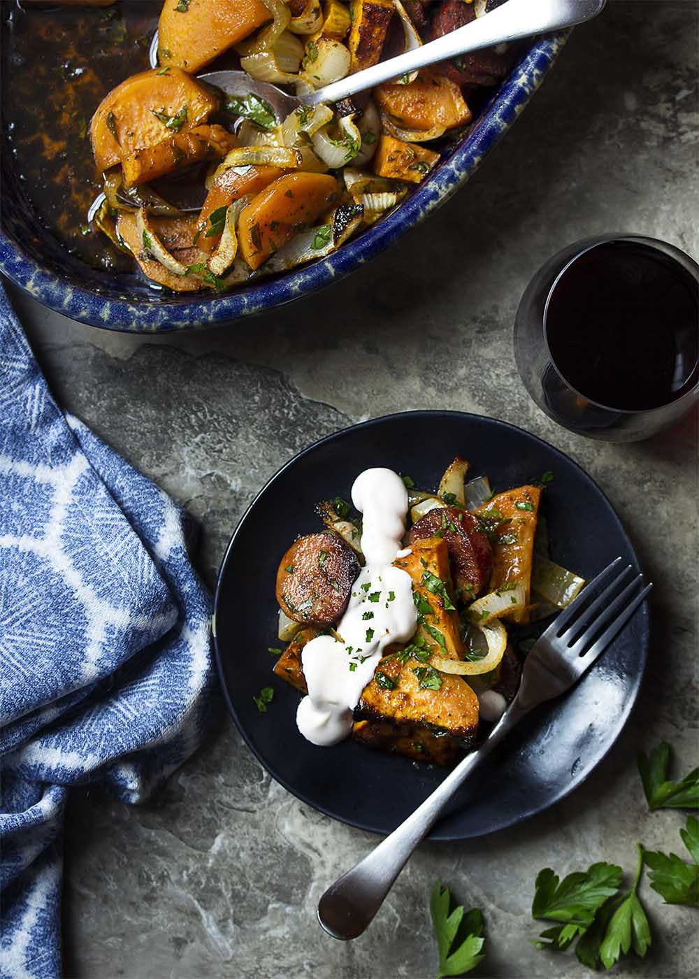 Table view of a plate and a casserole dish of baked chorizo and sweet potatoes.