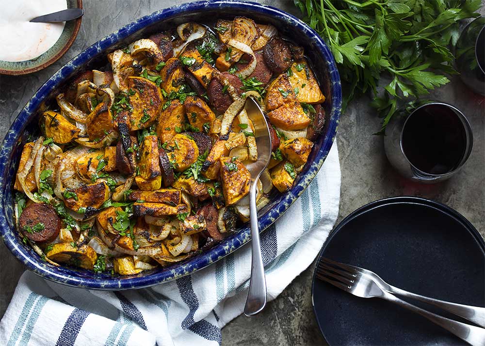 Table view of a casserole dish of baked sweet potatoes, onions, and chorizo showing the crispy top and tender potatoes.