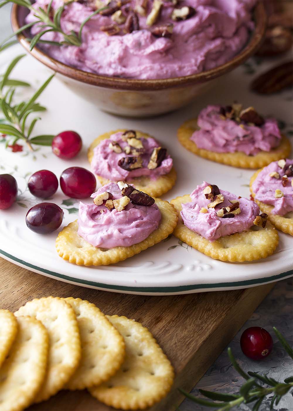 A platter of crackers topped with cranberry spread and toasted pecans.