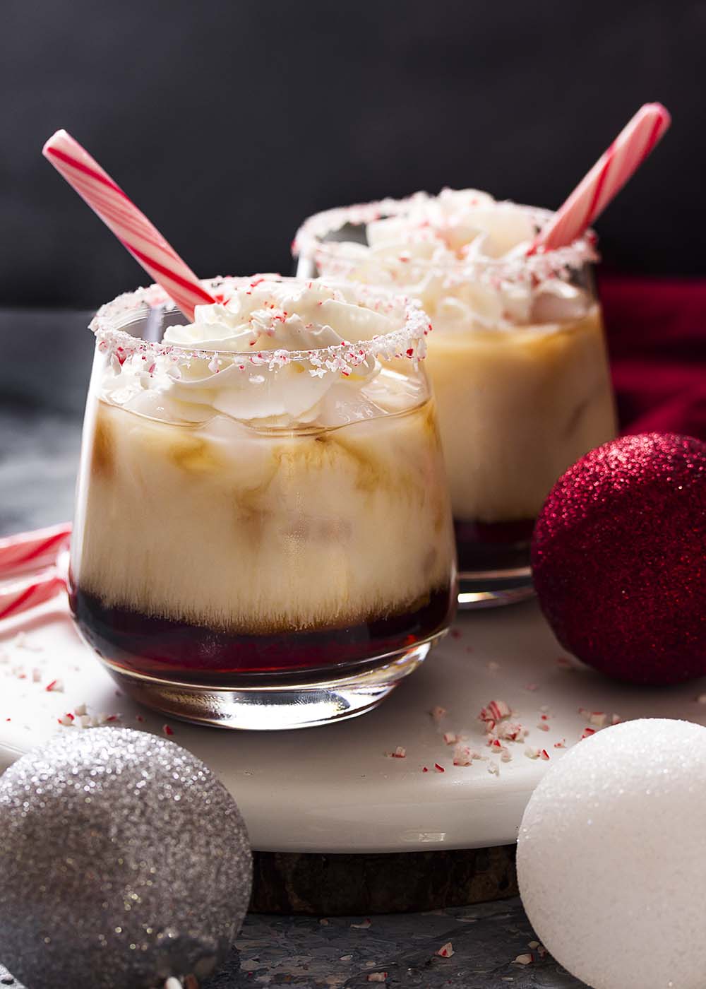 Two glasses of holiday cocktails each over ice with whipped cream and peppermint.
