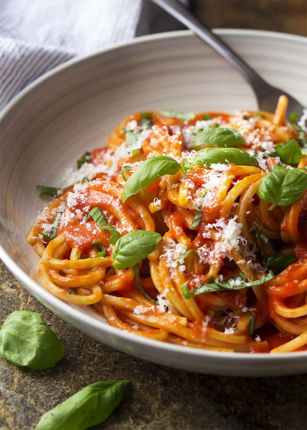 Close up of a wide bowl of spaghetti and tomato sauce with basil.