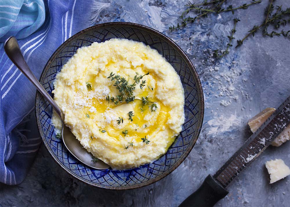 Top view of a bowl of soft polenta topped with butter, parmesan, and thyme.