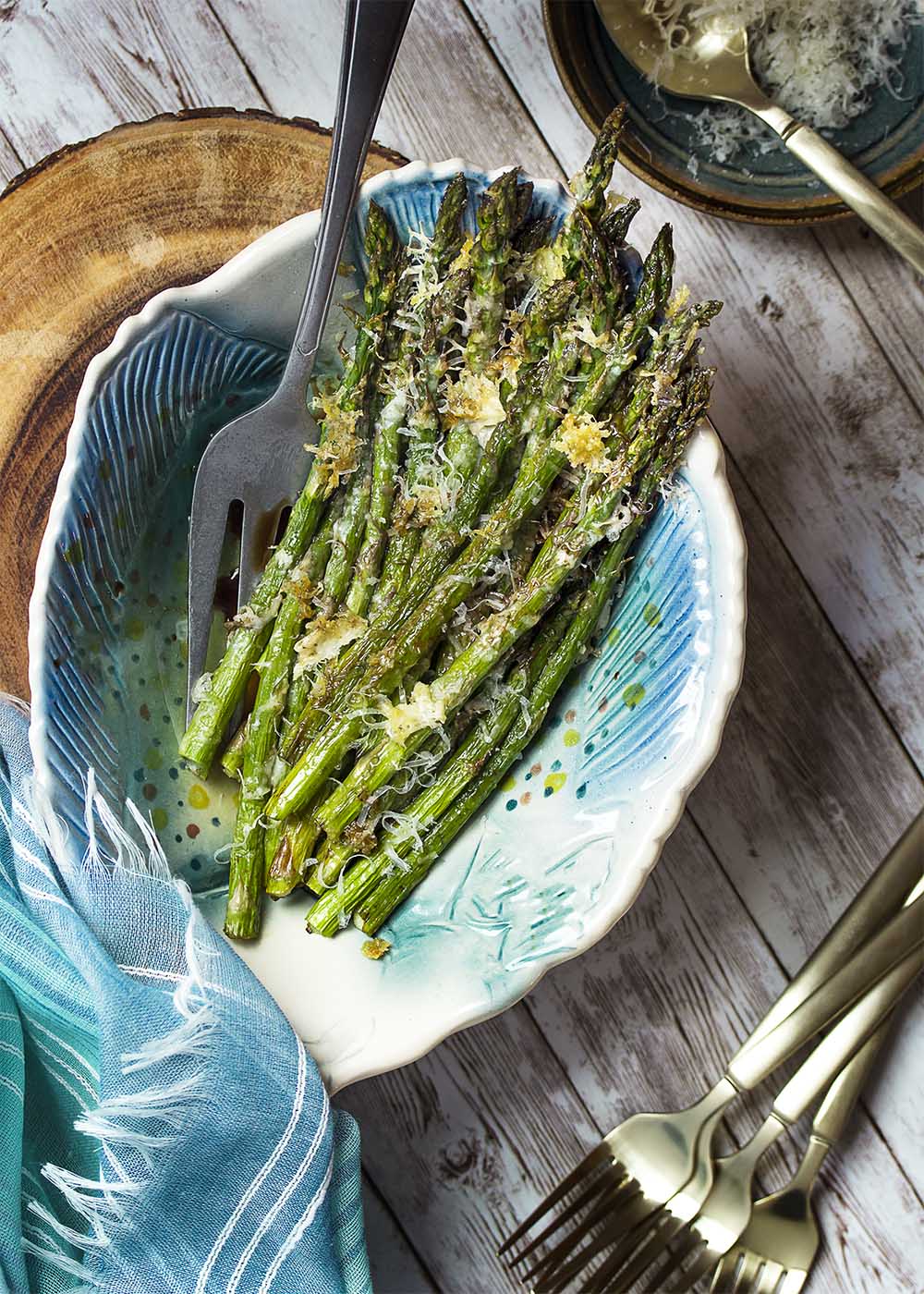 A serving bowl filled with roasted asparagus topped with crispy parmesan.