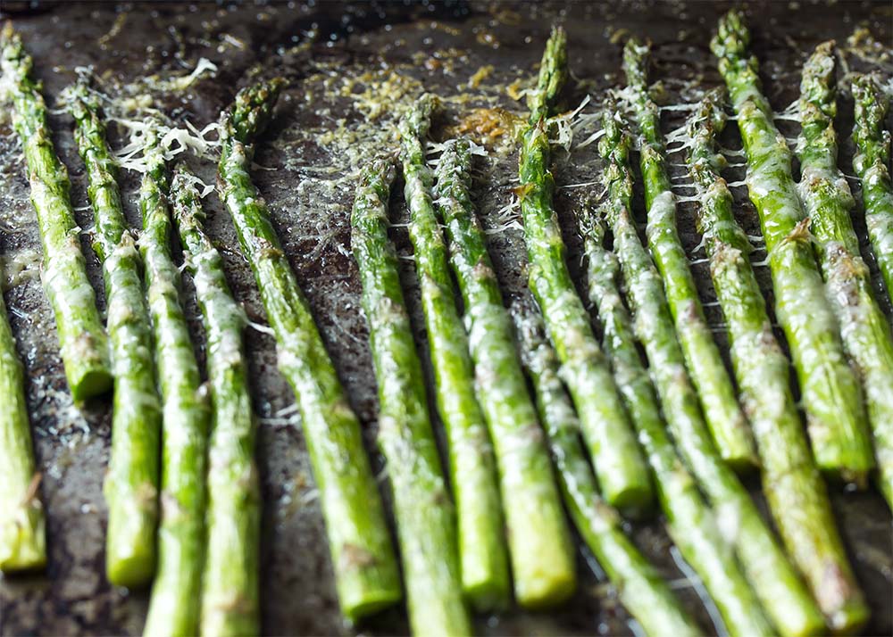 Asparagus spears lined up on a baking tray and topped with parmesan.