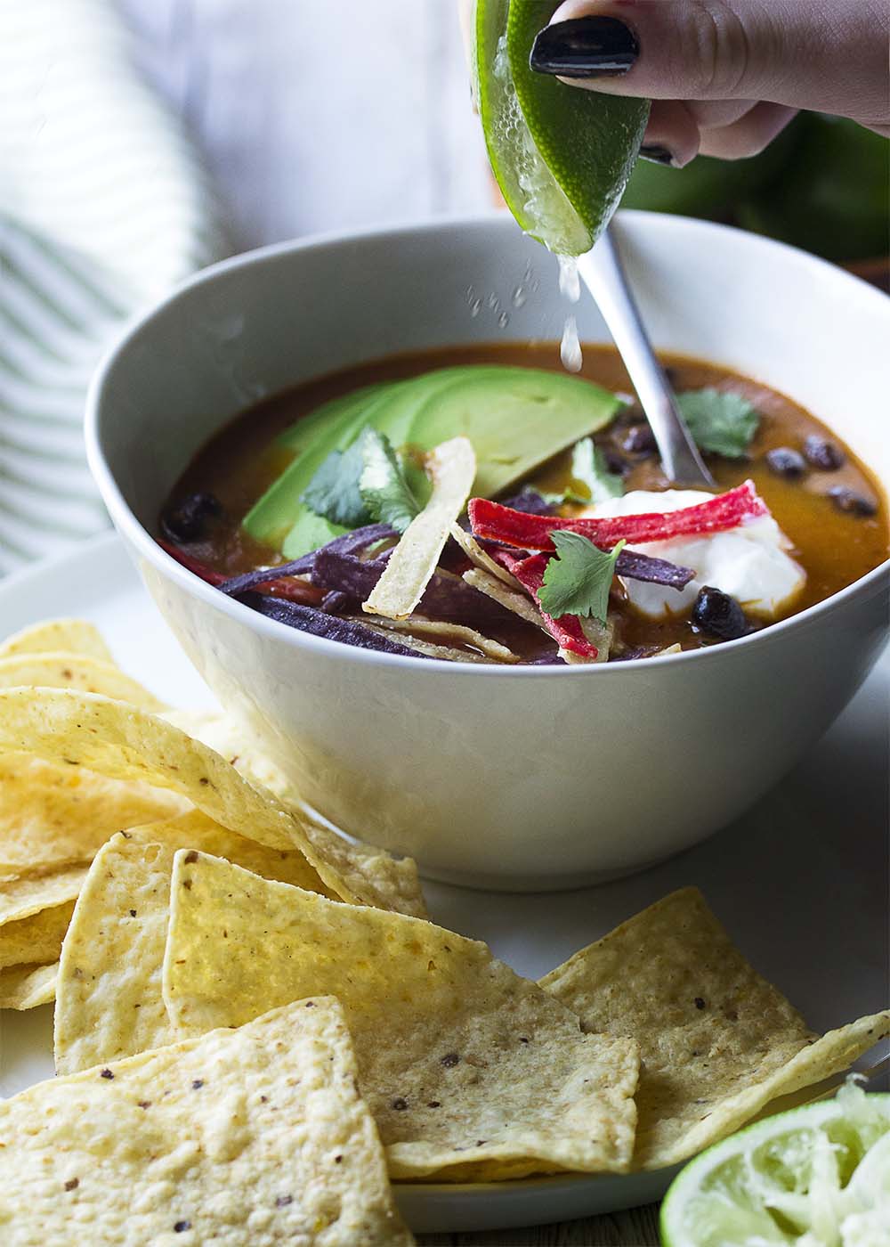 A hand squeezing a lime into a white bowl of vegetarian tortilla soup.