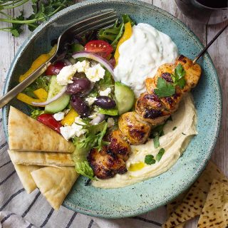 Enjoy Greek and Mediterranean flavors in my hummus bowl topped with marinated and grilled chicken souvlaki skewers, a green salad, tzatziki sauce, and crisp pita bread triangles. | justalittlebitofbacon.com #greekfood #mediterraneanfood #hummus #chickensouvlaki #greekdinners #grilledrecipes