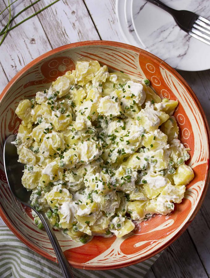 My creamy potato salad with peas and horseradish is tossed with sour cream and mayonnaise. Easy, homemade, and simple! Top with chives for extra zip. | justalittlebitofbacon.com #saladrecipes #potatosalad #potatorecipes #summerrecipes #bbqrecipes #summer #potatoes