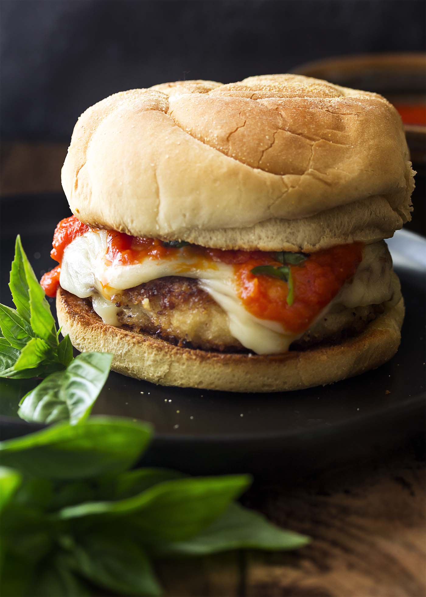 Chicken parm burger on a bun topped with melted mozzarella and tomato sauce.
