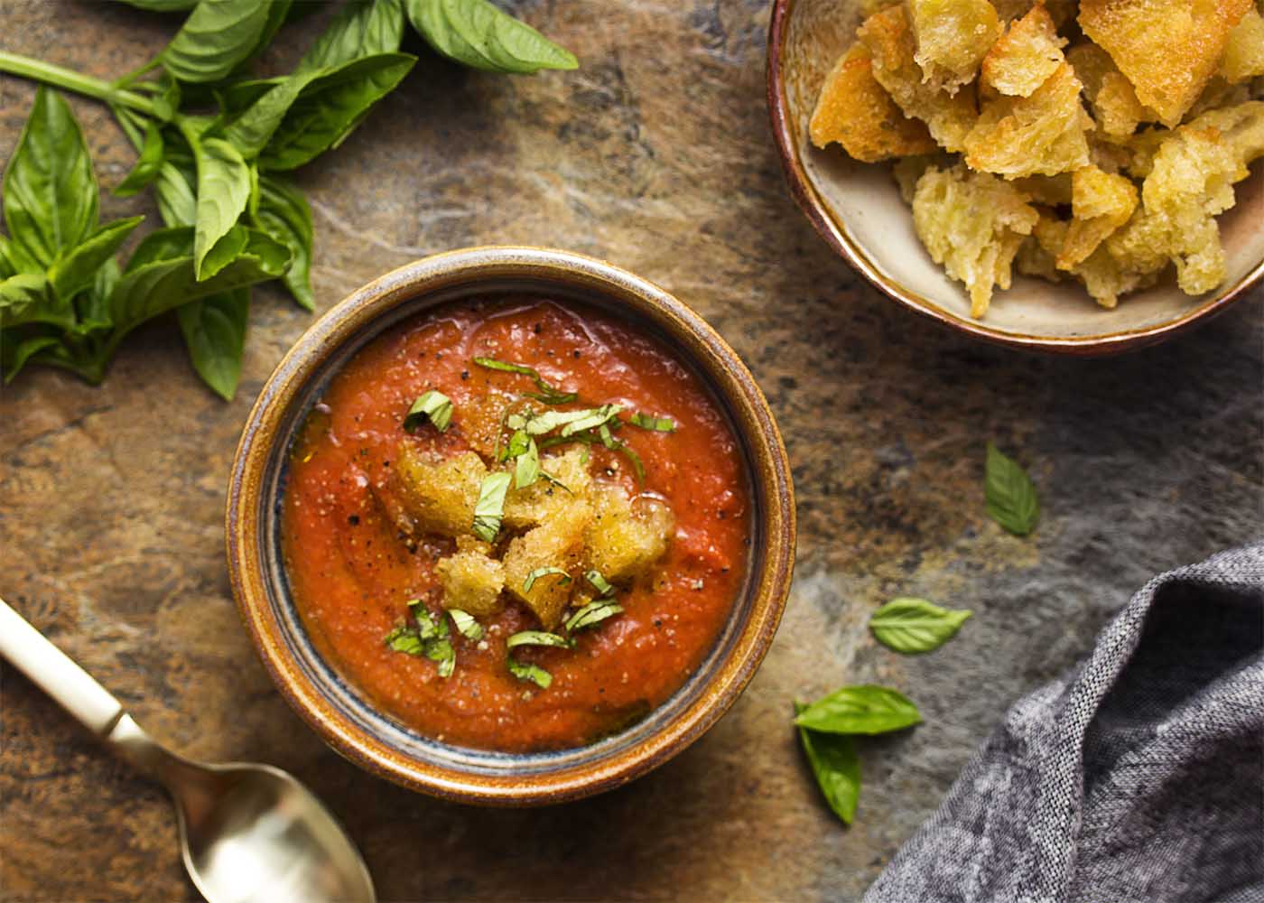 Top view of a bowl of tomato soup topped with croutons and basil.