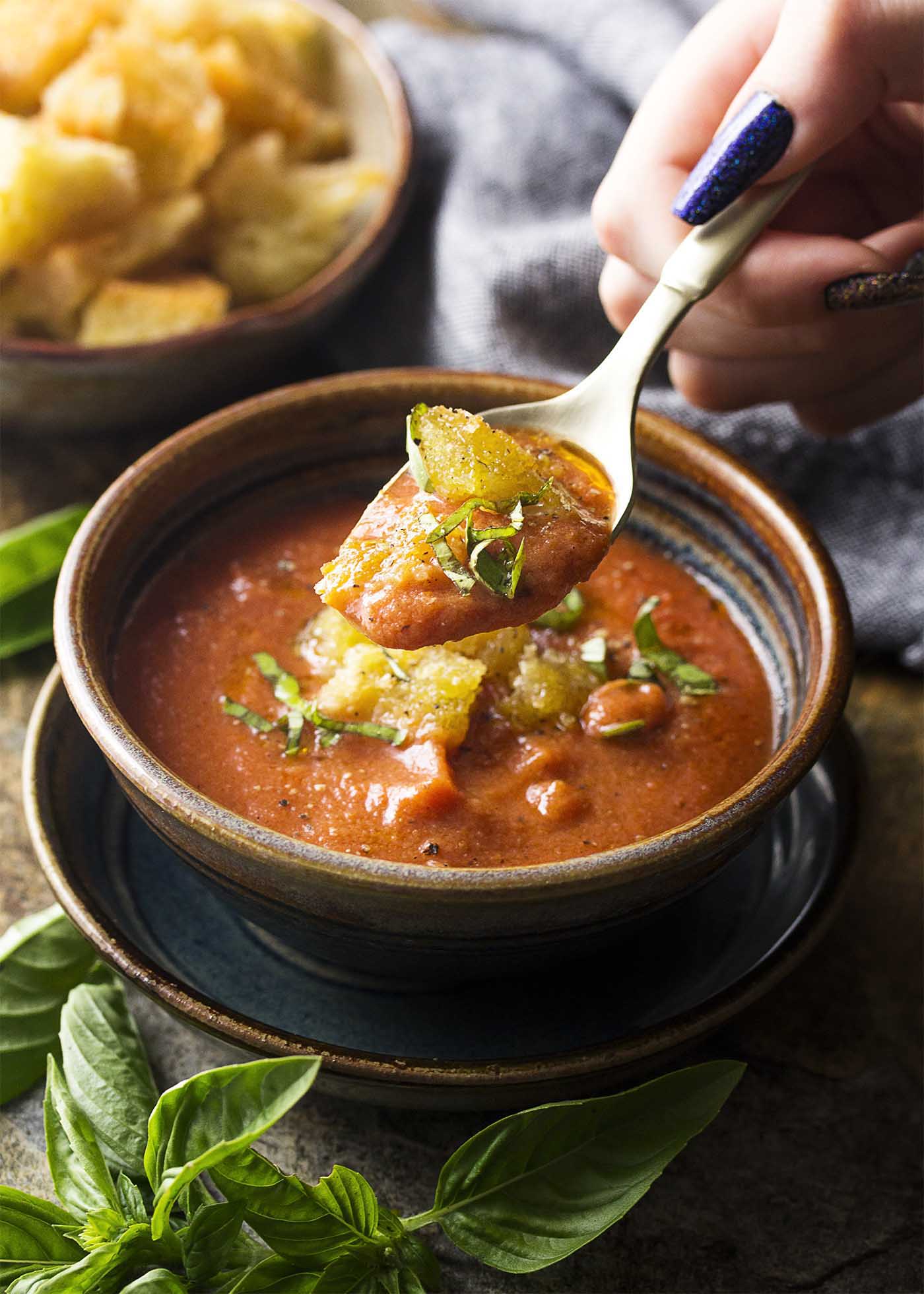 A hand holding up a spoonful of salmorejo soup over the bowl.