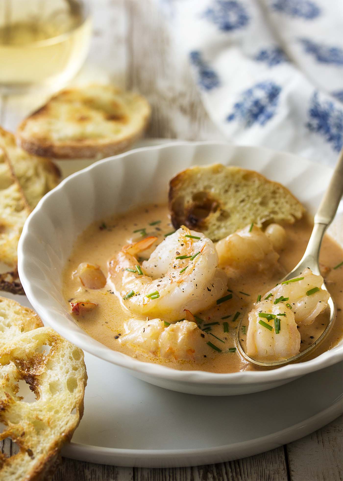 Creamy soup in a white bowl on a plate. Pieces of shrimp in the spoon.