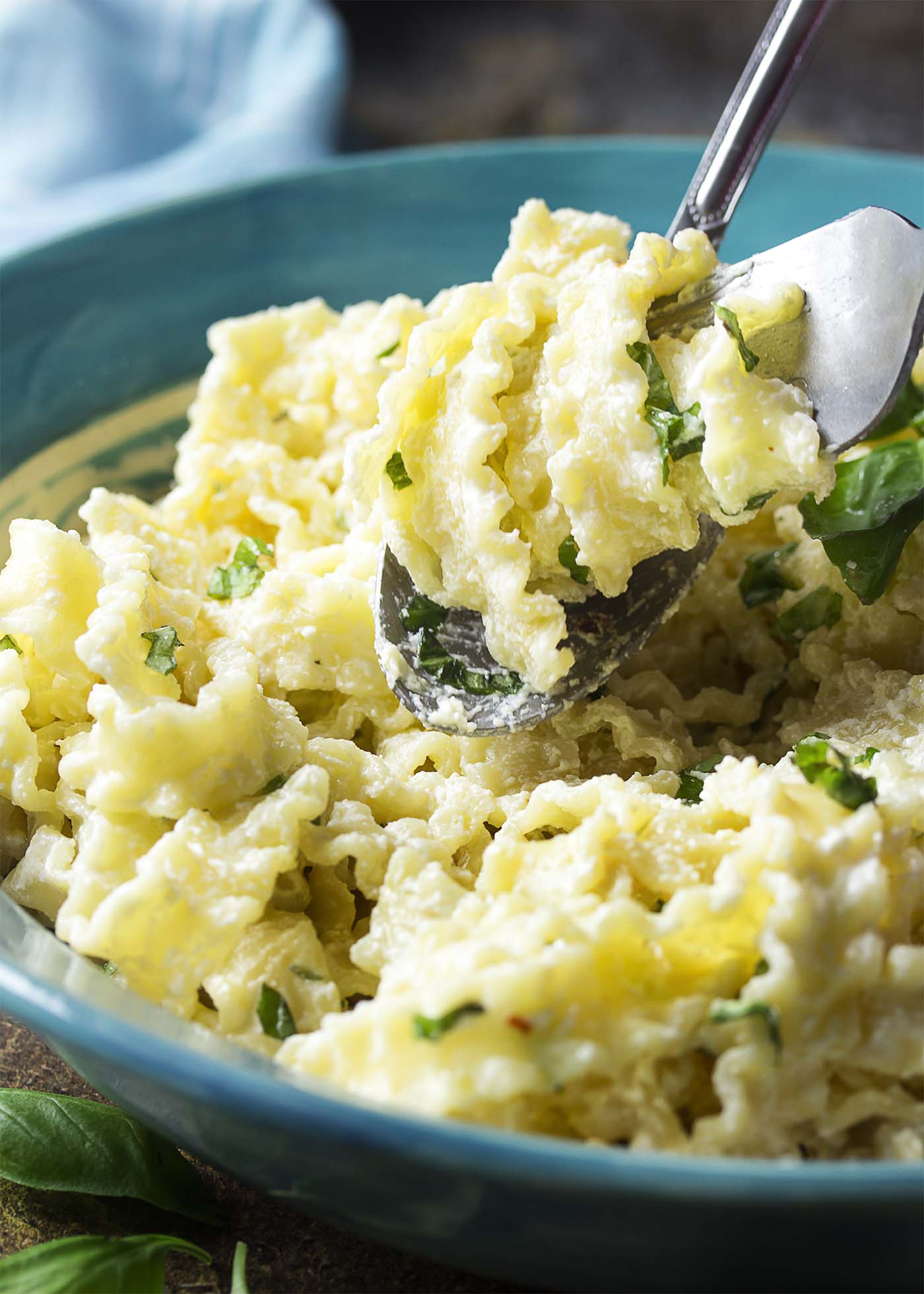 A fork and spoon dishing out some pasta tossed with a creamy sauce and fresh herbs.