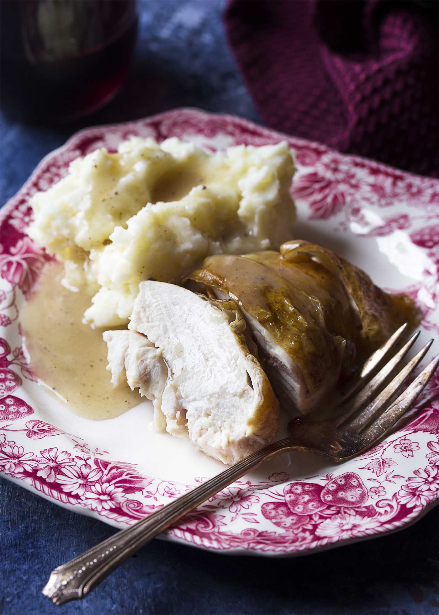 Sliced chicken breast, mashed potatoes, and gravy on a plate with fork.