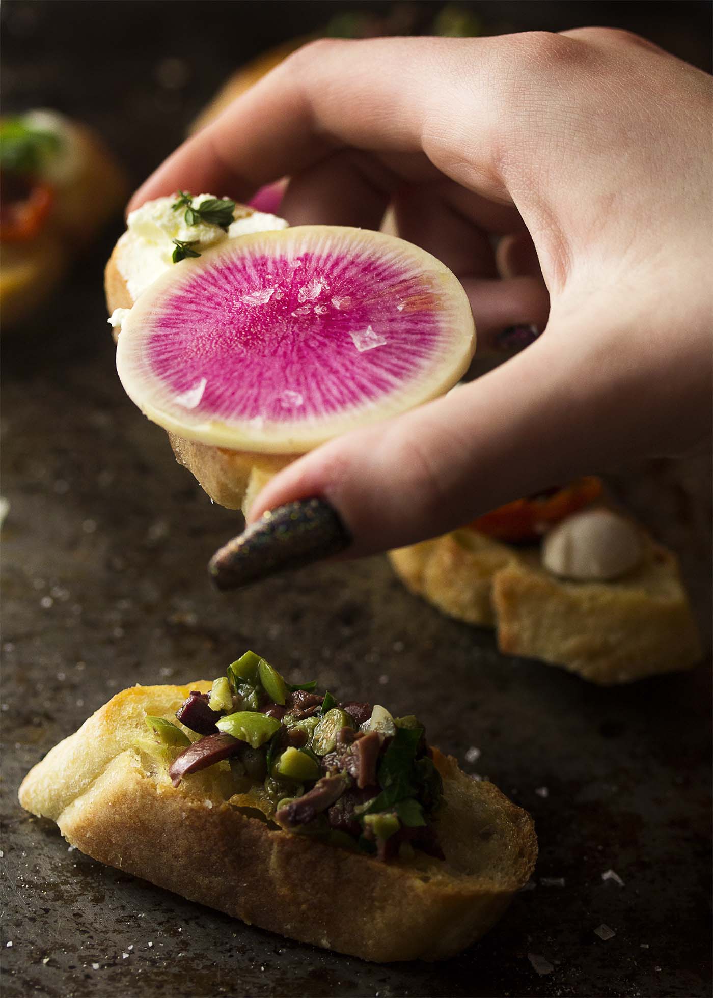 A hand holding up a crostini with goat cheese spread and a watermelon radish slice.