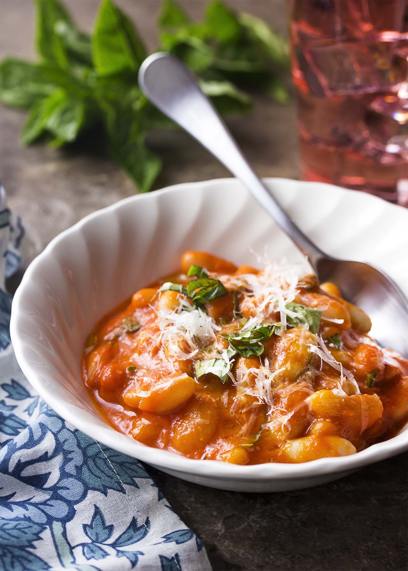 White bowl with a spoon. Bowl full of creamy white beans and pomodoro sauce topped by parmesan and herbs.
