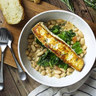 Have dinner in a bowl with pan seared halibut over creamy white beans and sauteed spinach! You'll love that this Mediterranean recipe is healthy, delicious, and quick. | justalittlebitofbacon.com #mediterraneanrecipes #halibut #fishrecipes #dinnerrecipes #easydinner