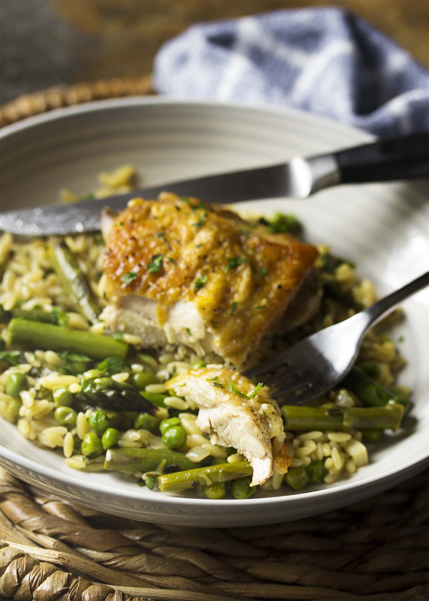 Chicken, orzo, and vegetables in a bowl with thigh cut open and a piece on a fork.