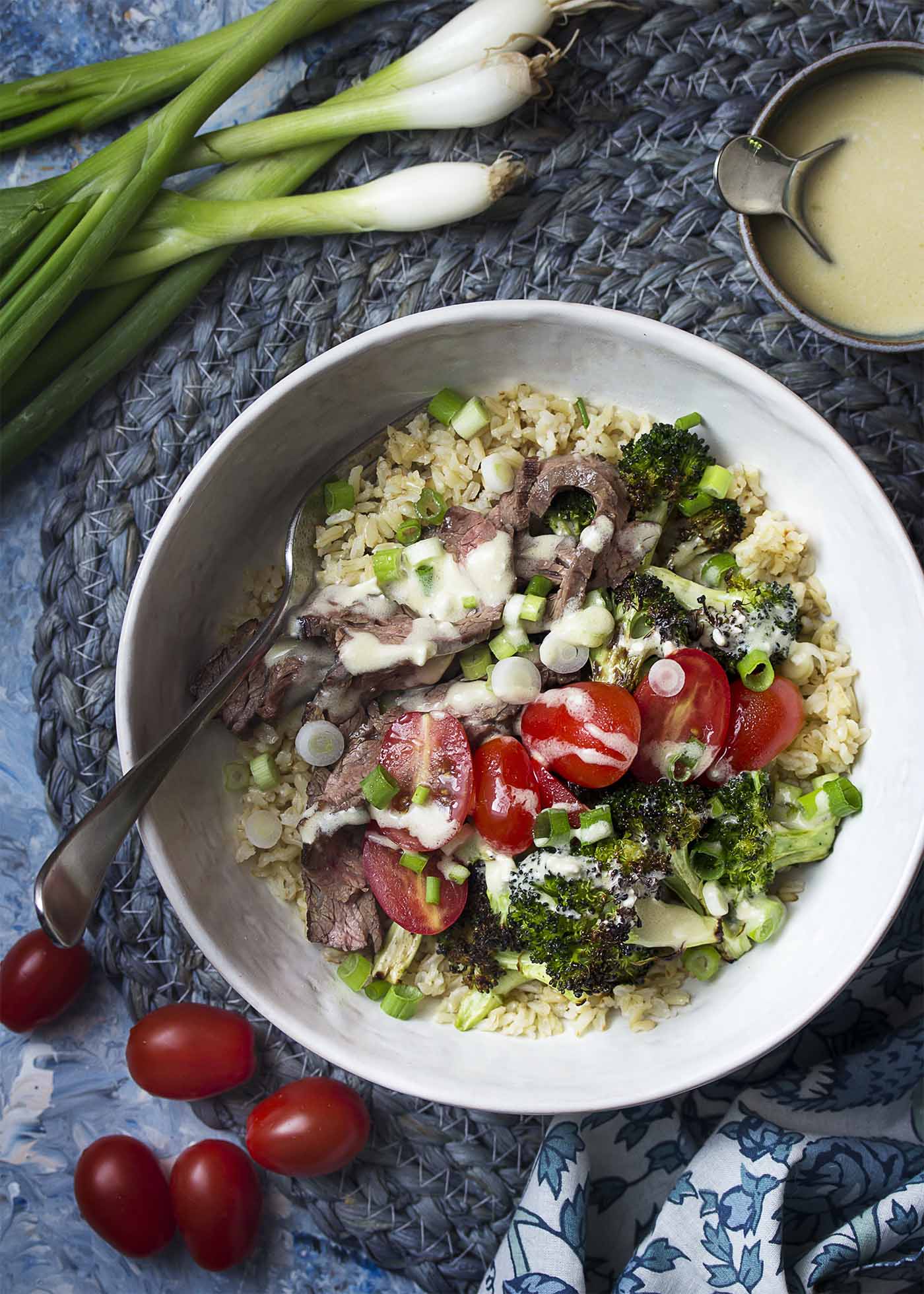 Top view of a grain bowl with brown rice, steak, and broccoli all topped by blue cheese.